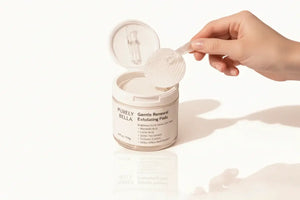 Hand holding a container of 'Purely Gentle Renewal Exfoliating Pads' with a white background