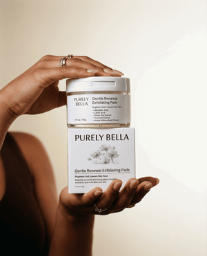 Hand holding a jar and box of Purely Bella Gentle Renewal Exfoliating Pads against a neutral background