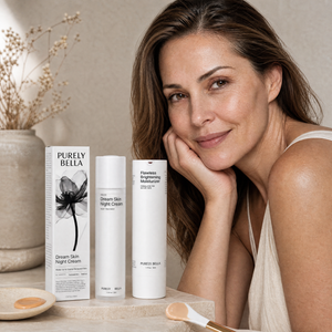 Woman leaning on a surface with Purely Bella skincare products in the foreground.
