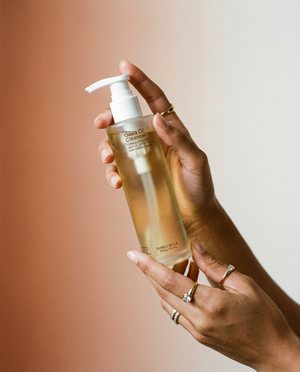 Hand holding a bottle of oasis oil Cleanser' with a pump against a warm-toned background