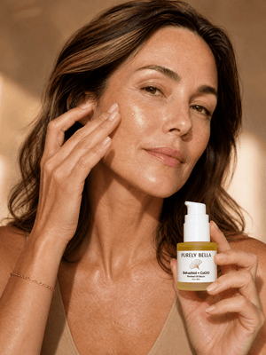 Woman applying skincare product to her face with a bottle labeled 'Purely Bella' in the background.