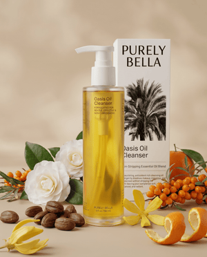 PURELY BELLA Oasis Oil Cleanser bottle and box surrounded by camellia flowers, sea buckthorn berries, and citrus peels.