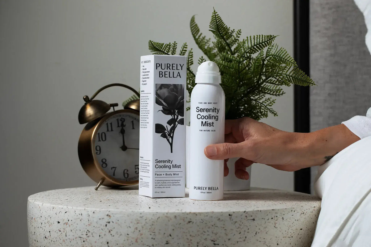 Hand holding Purely Bella Serenity Cooling Mist bottle with packaging on a table